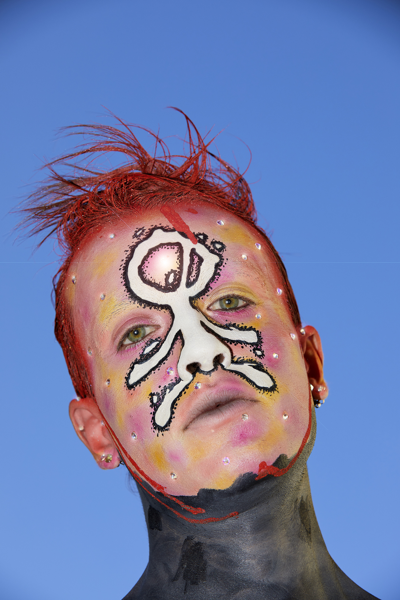 Portrait of Jesse in graphic red, white and black facepaint against a sky background